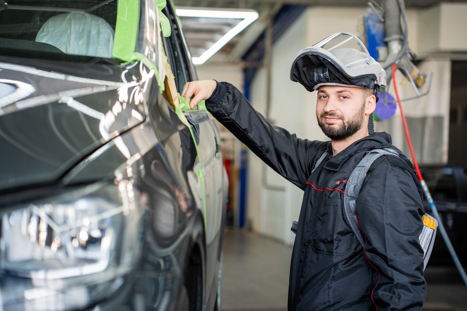 Lackierer mit Vollhelm und Akku-Frischluftsystem beim Abkleben eines Fahrzeugs in der Lackierkabine der Richter GmbH